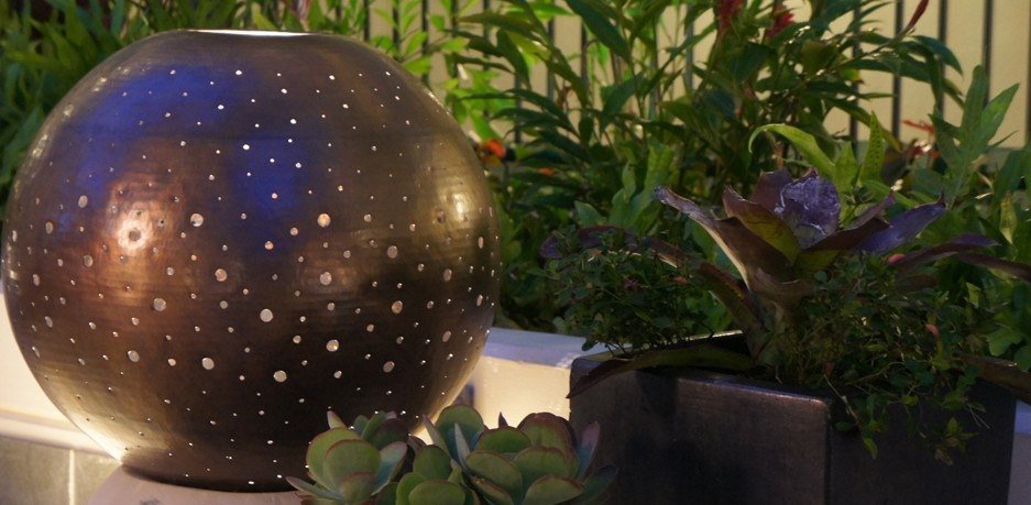 Pierced metal sphere lantern glowing among bromeliads at Allure Waikiki