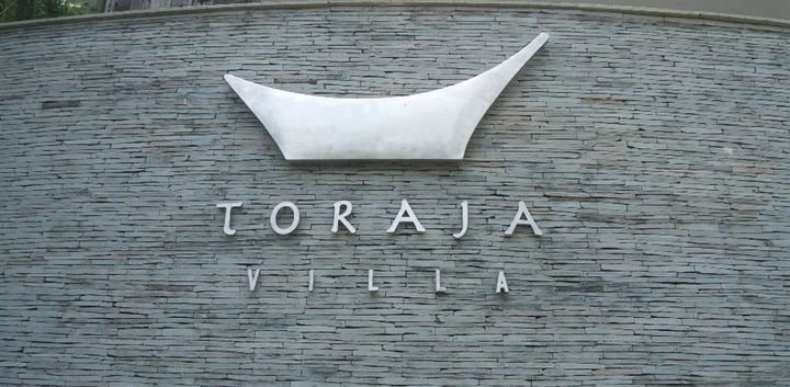 Carved lettering reading Toraja Villa set into a stacked stone wall, Bali